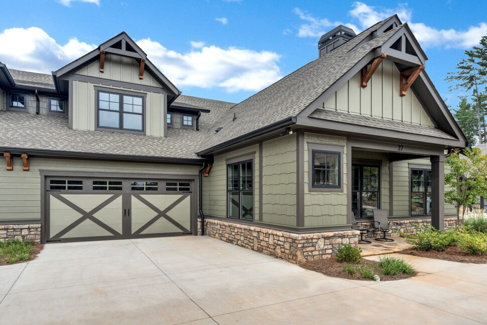 Modern craftsman-style with stone accents, sage-green siding, and double garage doors under a gabled roof.
