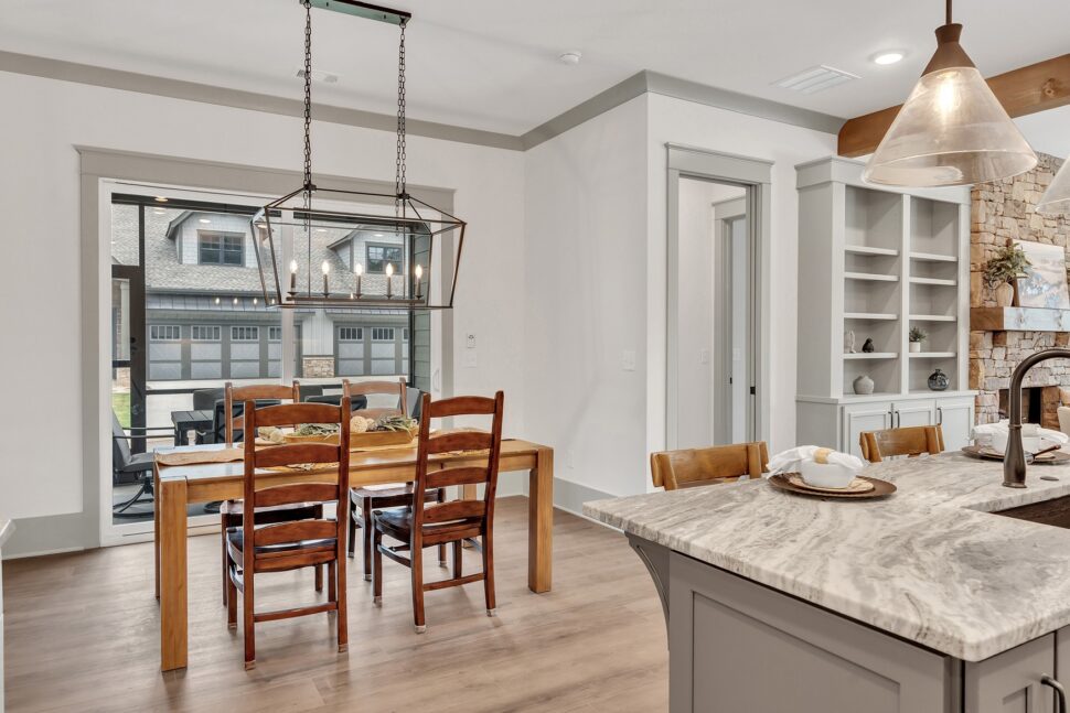 Dining room with wood table and modern chandelier overlooking patio and garage view through large glass door.