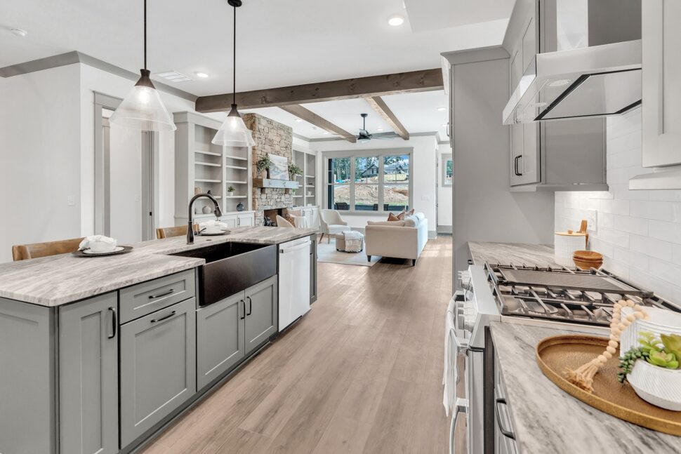 Modern kitchen with marble-style counters and black farmhouse sink opening into living area with stone fireplace.