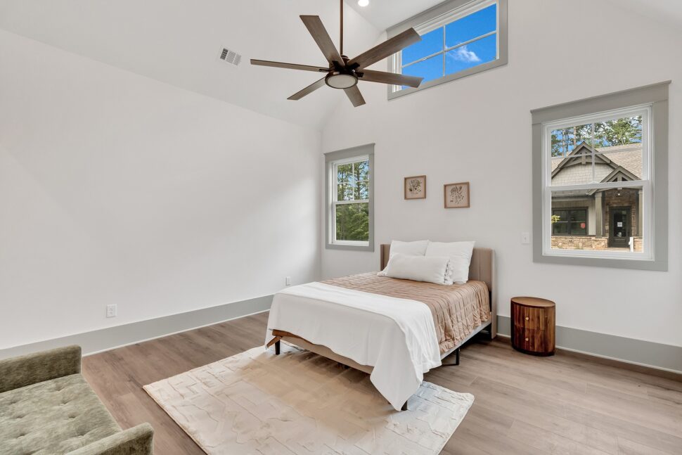 Bright primary bedroom with vaulted ceiling, large windows, neutral décor, and modern ceiling fan.