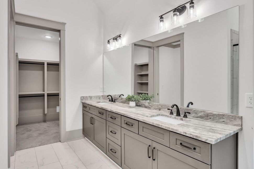 Modern bathroom with double-sink vanity, marble-style countertops, and view into spacious walk-in closet.