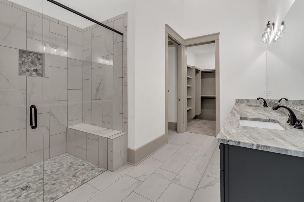 Luxury bathroom featuring glass-enclosed walk-in shower with tile walls, bench seating, and dual vanity.