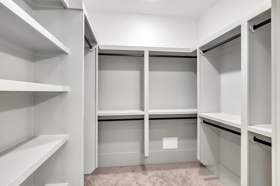 Large walk-in closet with built-in shelving, hanging rods, and soft carpet flooring.