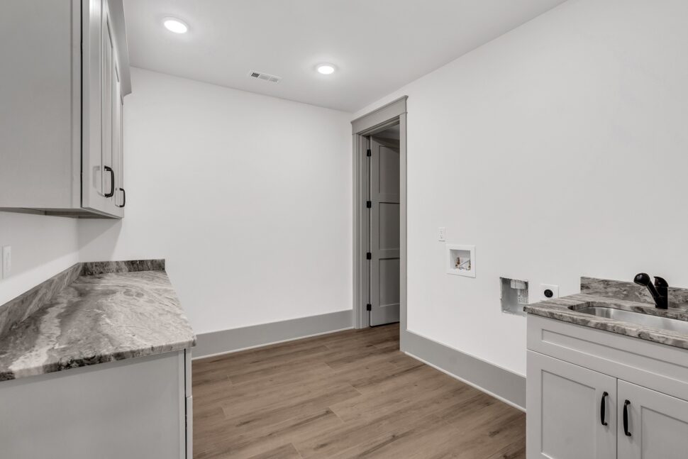 Laundry room with gray cabinetry, marble-look countertops, sink, and wood-style flooring.