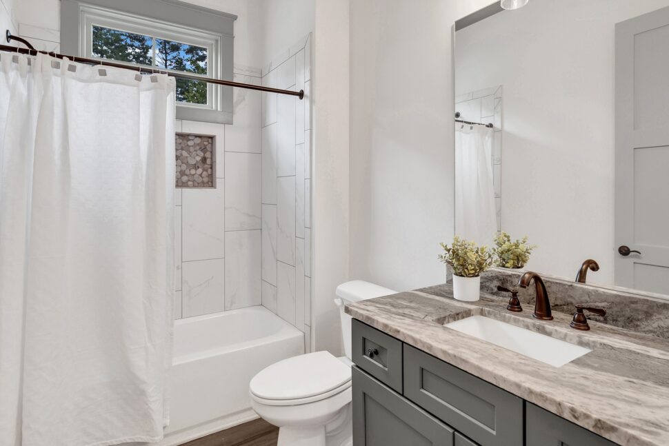 Guest bathroom with tile shower-tub combo, marble-style vanity, and bronze fixtures.
