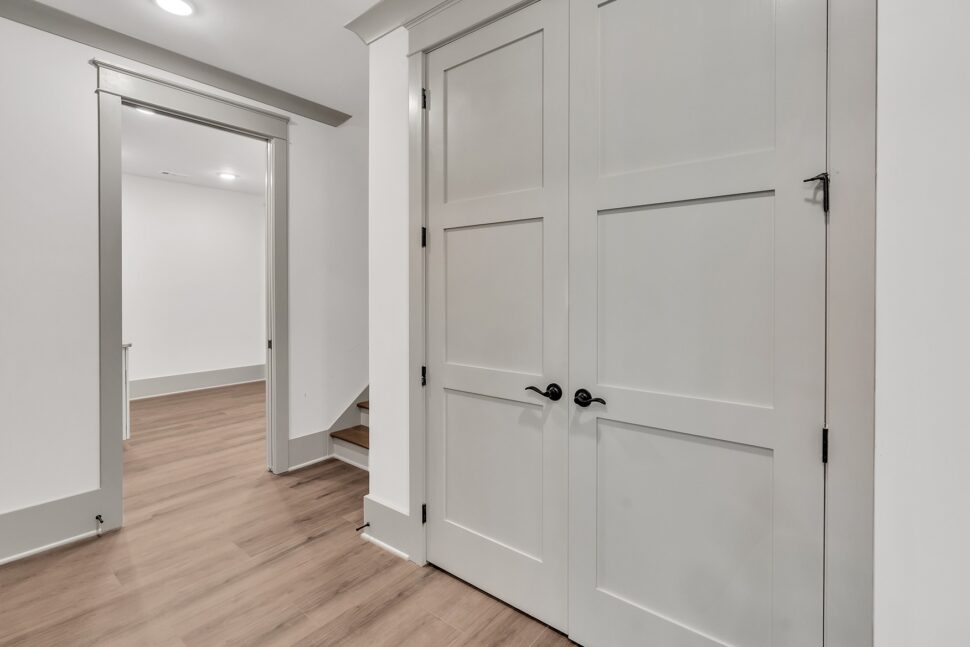 Hallway view with double gray doors and open doorway leading toward stairs and lower level.