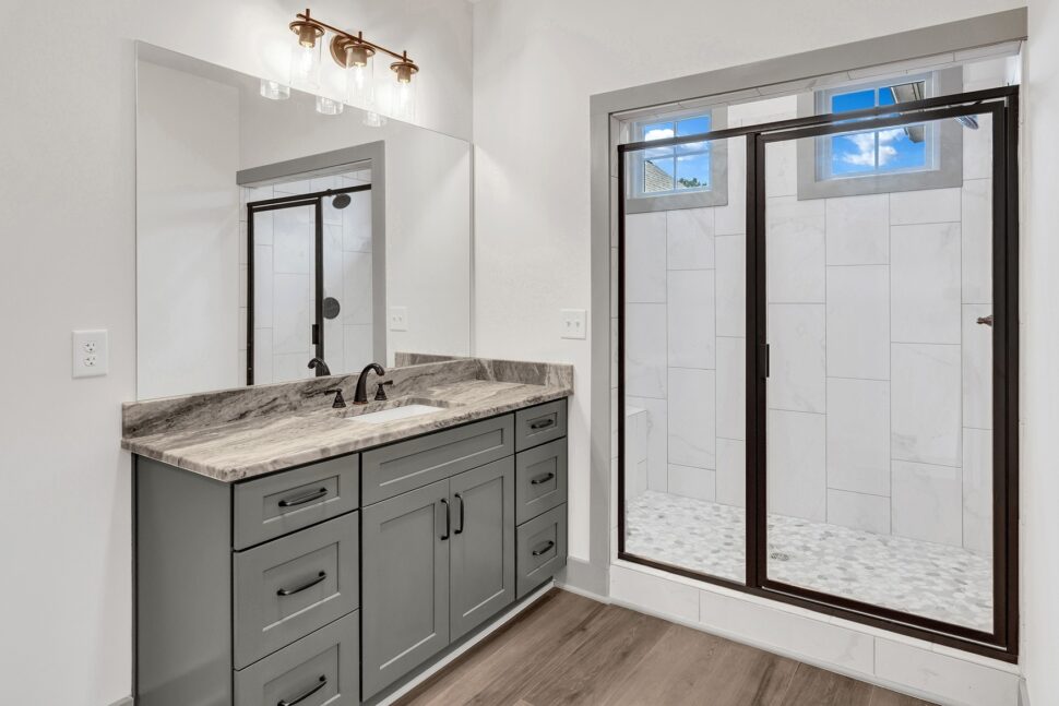 Contemporary bathroom with gray vanity, marble-style counter, and glass shower enclosure with tile walls.