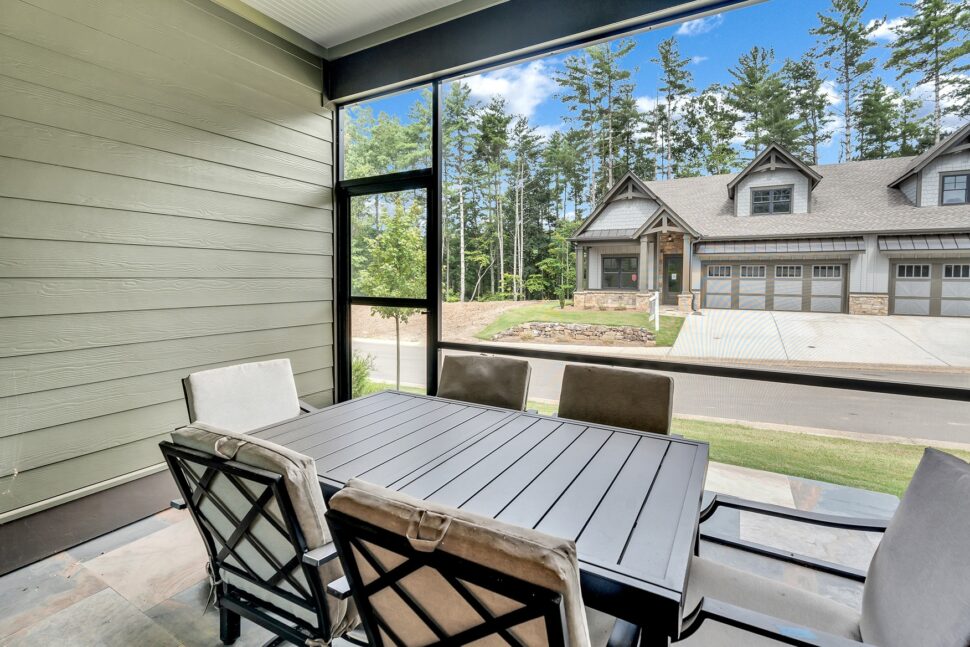 Screened-in patio with dining table and chairs overlooking neighboring Cottonwood Condos and wooded backdrop.